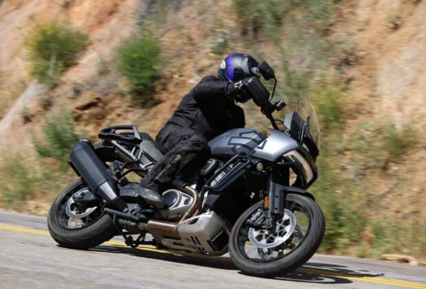 A rider leans into a turn on a Harley Davidson Pan America 1250 motorcycle on a winding road, 2K Desktop Wallpaper