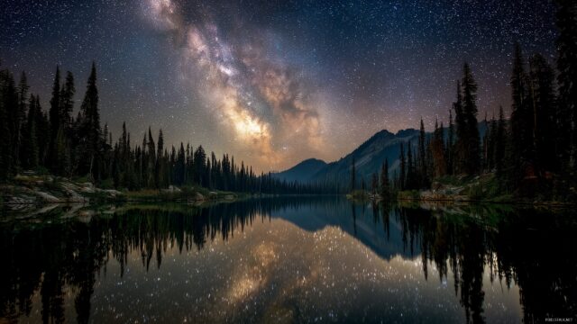 High res wallpaper HD landscapes, a serene lake surrounded by lush forests under a starry night sky with a reflection on the water.