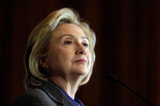 A focused portrait of Hillary Clinton speaking at a microphone with a dark background, 2K Desktop Wallpaper