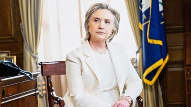 Hillary Clinton is sitting on a wooden chair in an office setting with a flag behind her, HD Desktop Wallpaper