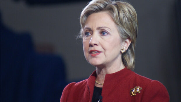 Hillary Clinton speaks during a public event wearing a red jacket and gold accessories, HD Desktop Wallpaper
