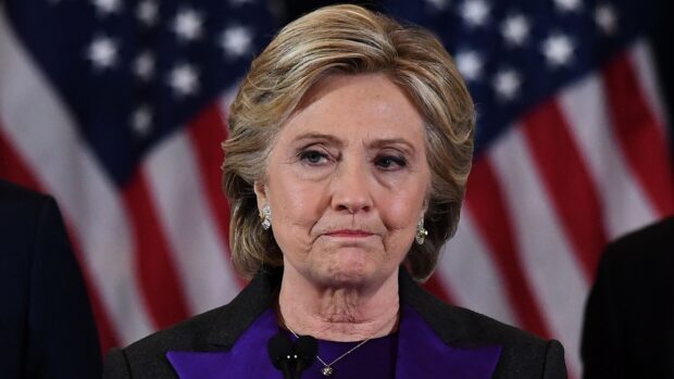 Hillary Clinton stands with a serious expression during a speech with American flags behind her, HD Desktop Wallpaper
