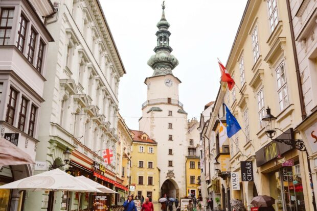 A busy street scene with Michael's Gate tower surrounded by buildings in Bratislava, HD Desktop Wallpaper