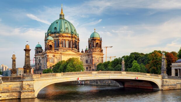 A historic cathedral with a green dome and stone bridge over the river under a blue sky, 4K Desktop Wallpaper