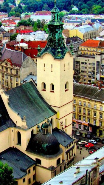 The historic church tower stands prominently in the cityscape of Ukraine, surrounded by traditional buildings and greenery, HD Mobile Wallpaper