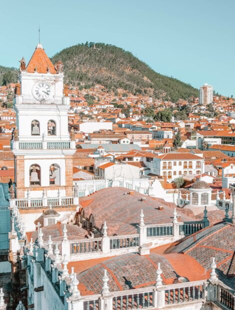 The image shows a historic clock tower overlooking the cityscape surrounded by mountains in Bolivia, HD Desktop Wallpaper