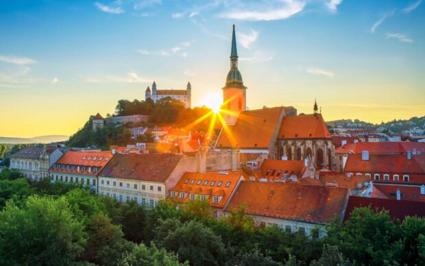 The historic skyline of Bratislava features a castle and church with the sun setting behind them, HD Desktop Wallpaper