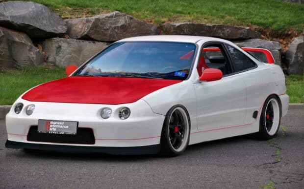 A white and red Honda Integra is parked on a paved road with a rocky and grassy background, 2K Desktop Wallpaper