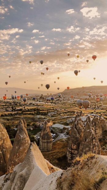 The Cappadocia Wallpapers show dozens of colorful hot air balloons flying over unique rock formations and a scenic landscape, HD Mobile Wallpaper