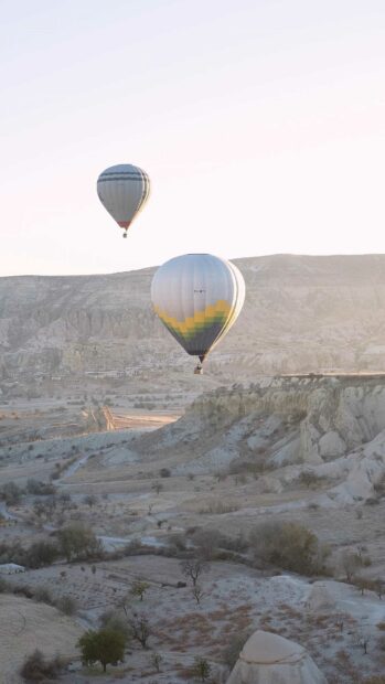 Two hot air balloons float above the rocky terrain of Cappadocia in a peaceful morning scene, 4K Phone Wallpaper