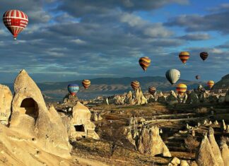 Hot air balloons drift above the iconic rock formations in Cappadocia during a clear morning, 2K Desktop Wallpaper
