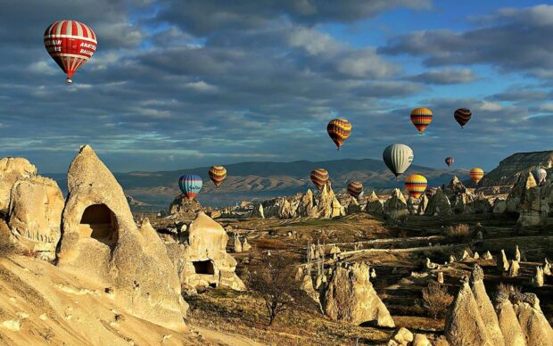Hot air balloons drift above the iconic rock formations in Cappadocia during a clear morning, 2K Desktop Wallpaper