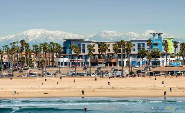 Huntington Beach Scenic View with Snowy Mountains and Vibrant Waterfront Buildings Wallpaper