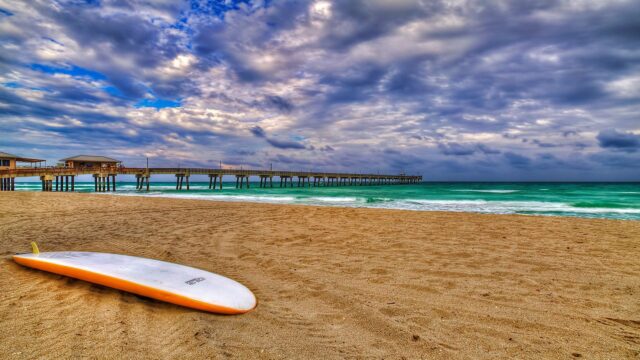 Huntington Beach Surfboard on Sandy Beach with Pier and Dramatic Sky Wallpapers