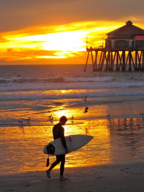Huntington Beach Wallpapers Surfer Walking Along the Shore at Sunset with Pier Background