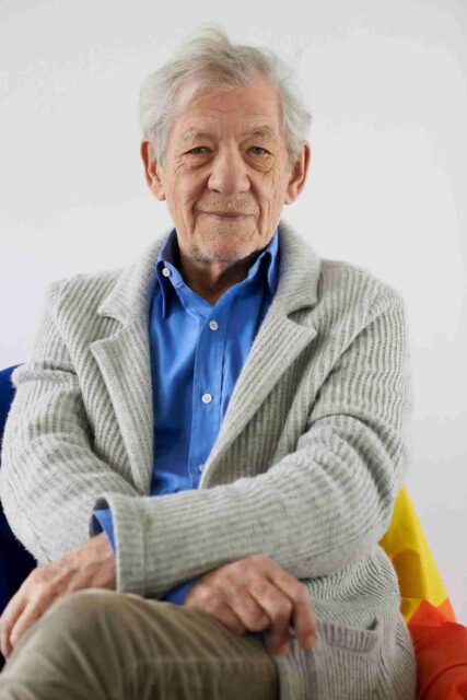 Ian McKellen Seated In Cozy Sweater And Blue Shirt Wallpaper For Fans