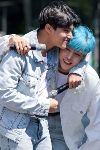 Two friends smiling and embracing with microphones in casual outfits, HD Mobile Wallpaper