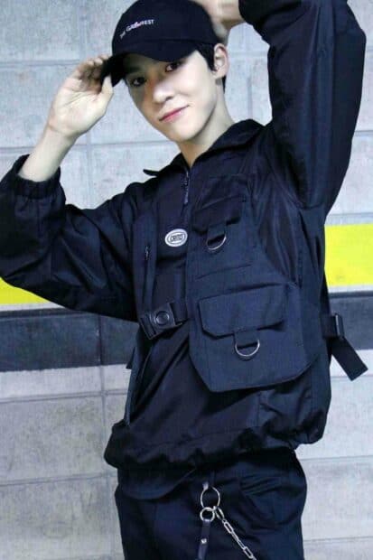 A young man named Jeong Yun Ho wears a black cap and vest while posing happily against a concrete wall, HD Mobile Wallpaper