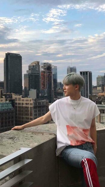 Jeong Yun Ho is sitting on a rooftop balcony with city buildings in the background, HD Mobile Wallpaper