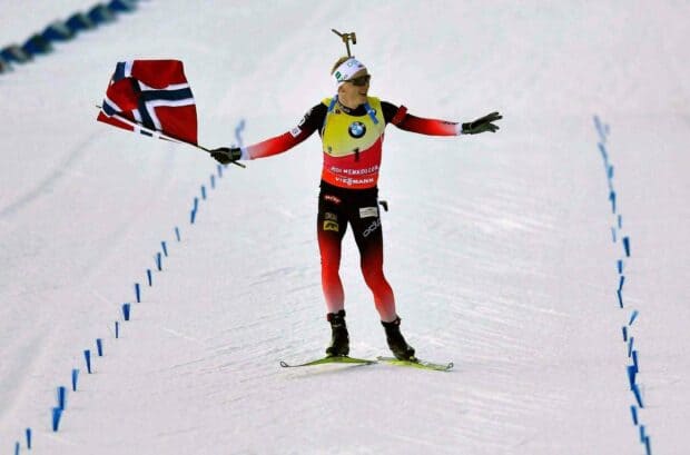 Johannes Thingnes celebrates on the snow with a Norwegian flag during a ski event, HD Desktop Wallpaper
