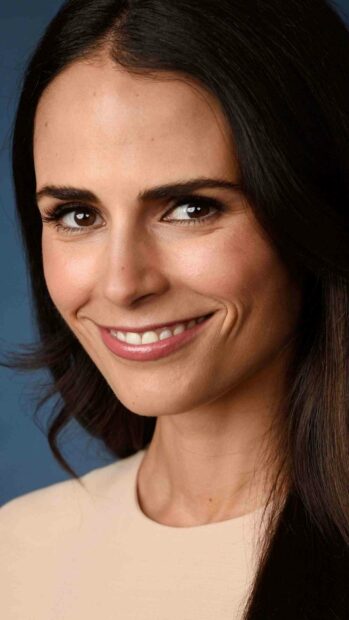 Jordana Brewster smiles gently in a close up portrait against a blue background, 2K Mobile Wallpaper