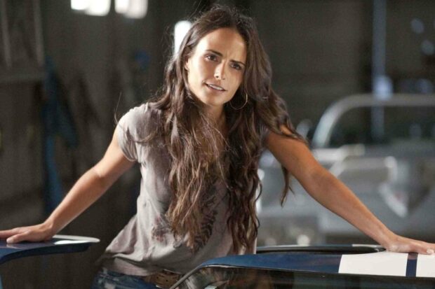 Jordana Brewster leans on a car with a focused expression in a garage setting, HD Desktop Wallpaper