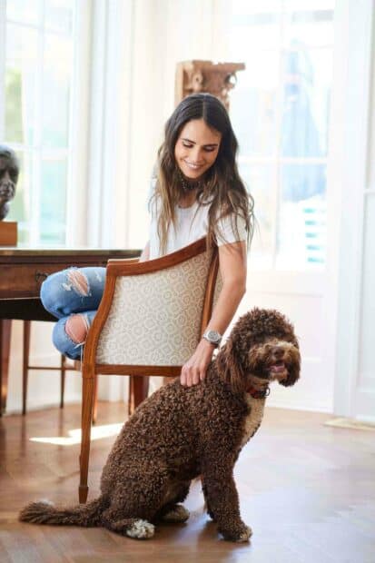 Jordana Brewster sitting on a chair petting her curly brown dog in a sunlit room, 2K Desktop Wallpaper