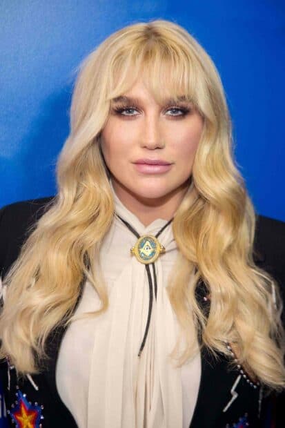 A close up portrait of Kesha with blonde wavy hair and blue eyes against a blue background, 2K Phone Wallpaper
