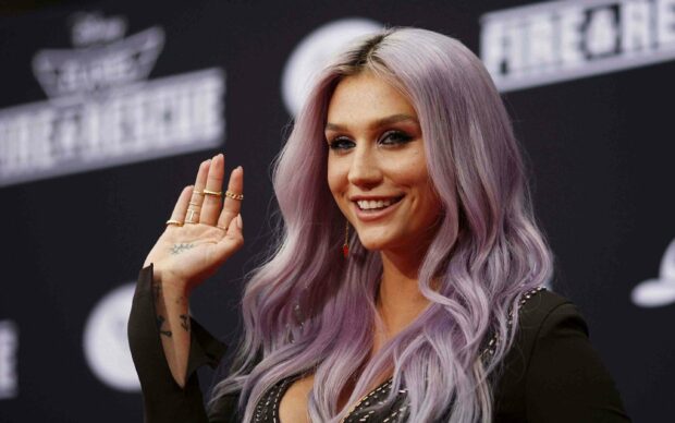 Kesha with long purple hair smiling and waving at a public event, 2K Desktop Wallpaper