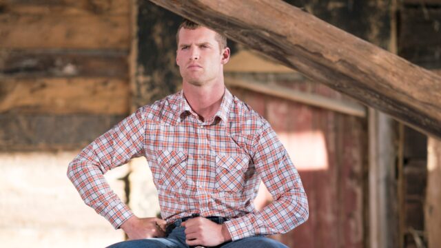 Letterkenny TV Series Wallpaper Featuring Man In Plaid Shirt Sitting In Rustic Setting