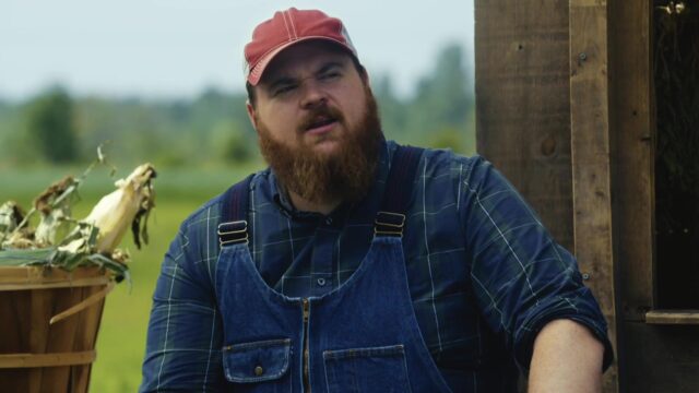 Letterkenny TV Series Wallpaper Featuring Bearded Man In Cap And Overalls Outdoors
