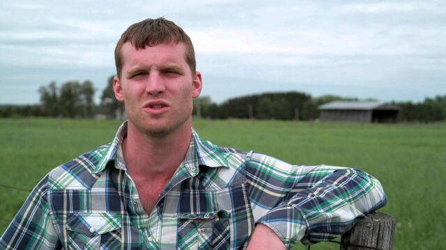 Letterkenny Tv Series Wallpaper Featuring Farmer In Plaid Shirt With Rural Background