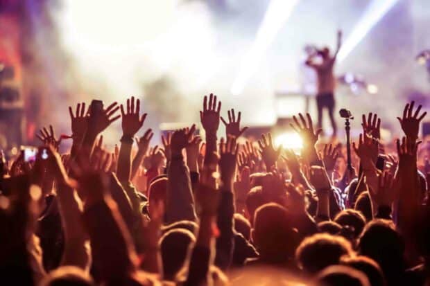 A lively crowd raises their hands at a concert with bright stage lights and a performer in the background, HD Desktop Wallpaper