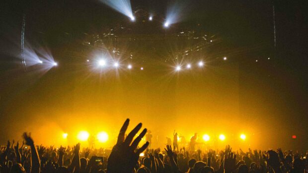 A lively crowd enjoying a live concert with bright yellow lights on stage and raised hands, 4K Desktop Wallpaper