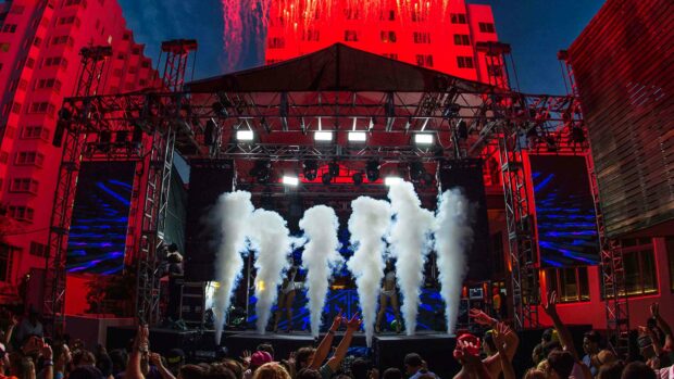 A live concert stage with smoke effects and a cheering crowd under vibrant red lighting, 4K Desktop Wallpaper