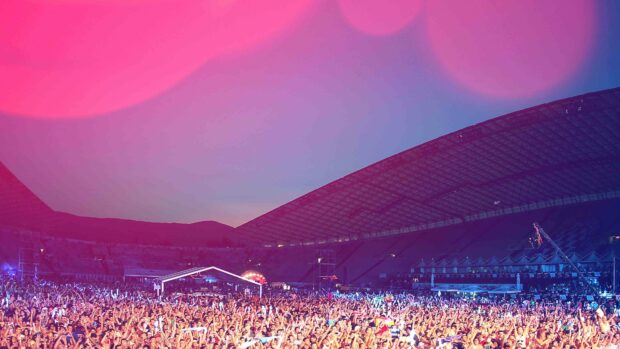 A large crowd is gathered in an open stadium enjoying a concert with vibrant lighting, 4K Desktop Wallpaper