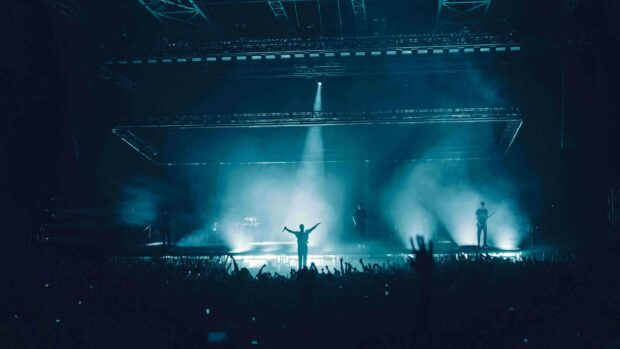 A live concert performance with a singer and band illuminated by stage lights and surrounded by an enthusiastic audience, 4K Desktop Wallpaper