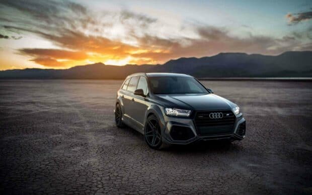 Luxury Audi Q7 at Sunset Desert   A luxury Audi Q7 is parked on a dry desert floor with mountains and a vibrant sunset in the background   2K Desktop Wallpaper