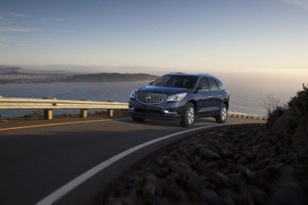 A Buick Enclave is driving on a winding coastal road with the ocean and hills in the background, 2K Desktop Wallpaper