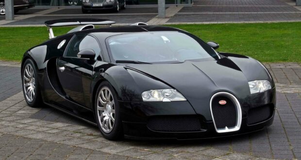 A luxury black Bugatti Veyron is parked outdoors on a paved area with green grass in the background, 2K Desktop Wallpaper
