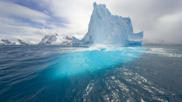 A large Arctic iceberg rises from the cold ocean under a cloudy sky, showcasing the beauty of Arctic landscapes, 4K Desktop Wallpaper
