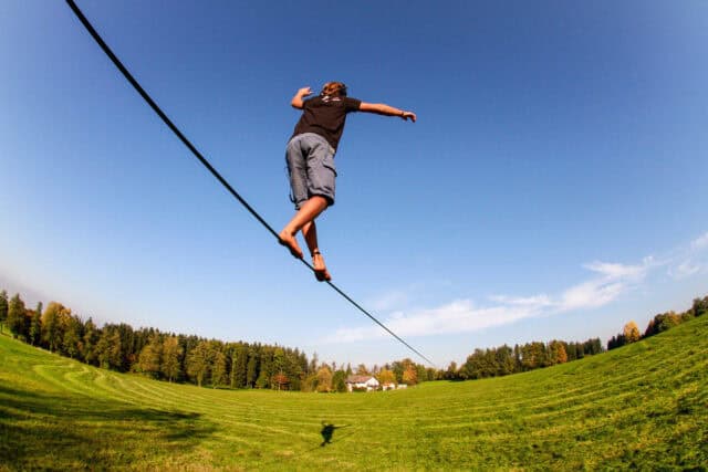 Man Balancing on Slackline Over Green Field Under Clear Blue Sky Slacklining Wallpapers