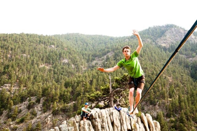 Man balancing on slackline above rocky cliff with forest background for slacklining wallpapers
