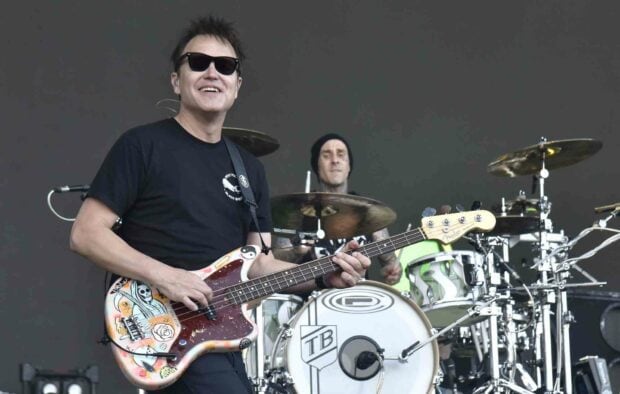 Mark Hoppus is smiling while playing guitar during a live performance with a drummer in the background, HD Desktop Wallpaper