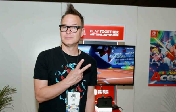 Mark Hoppus is posing with a peace sign in front of a Nintendo display at a gaming convention, HD Desktop Wallpaper