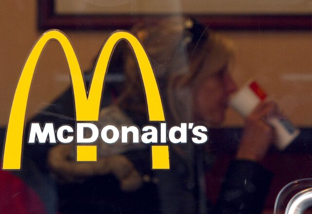 McDonalds logo on glass with blurred customer drinking inside restaurant background