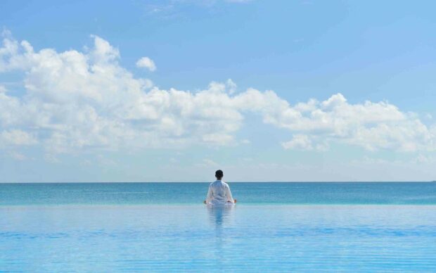 A person practicing yoga meditation facing the ocean under a clear sky, 2K Desktop Wallpaper