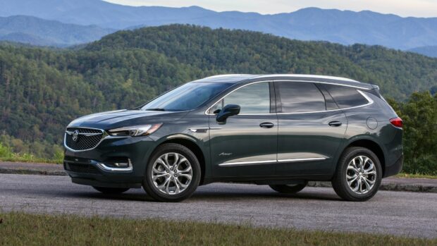 A sleek Buick Enclave is parked on the roadside with forested mountains in the background, 4K Desktop Wallpaper
