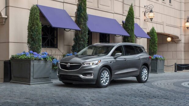 A sleek gray Buick Enclave is parked on a cobblestone street next to an elegant building with purple awnings and flowering plants, HD Desktop Wallpaper