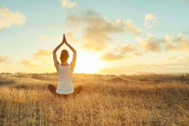 A woman is doing yoga in a seated pose facing the sunrise in a field, HD Desktop Wallpaper